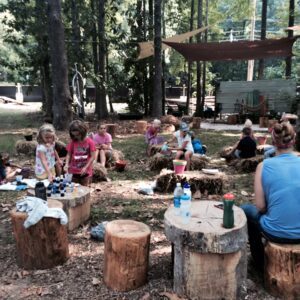 Children and adults engage in an outdoor group activity in a forest setting.